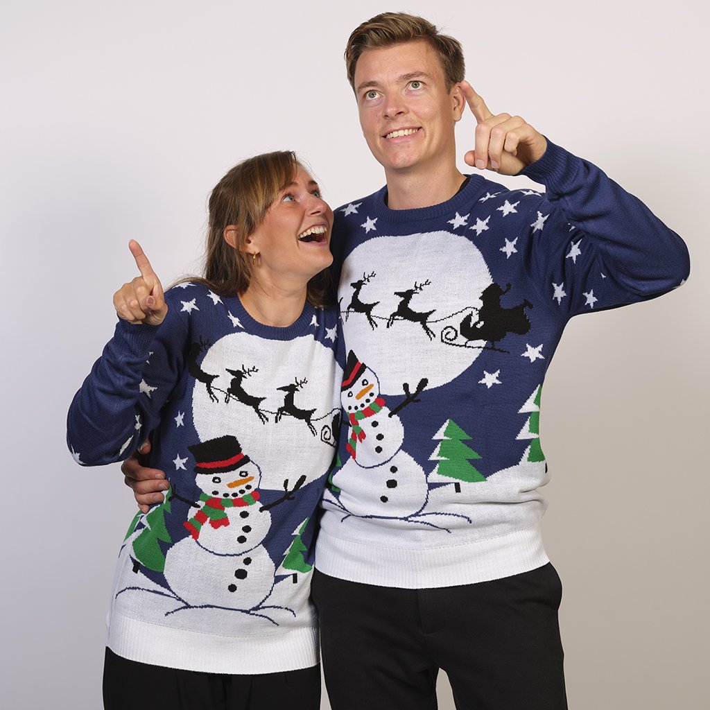 Una coppia che indossa un maglione natalizio blu con un pupazzo di neve e una luna.